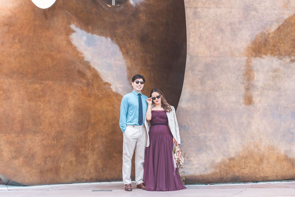 National Gallery of Art engagement photos of a couple posing in sunglasses in front of a large bronze sculpture outside the museum.