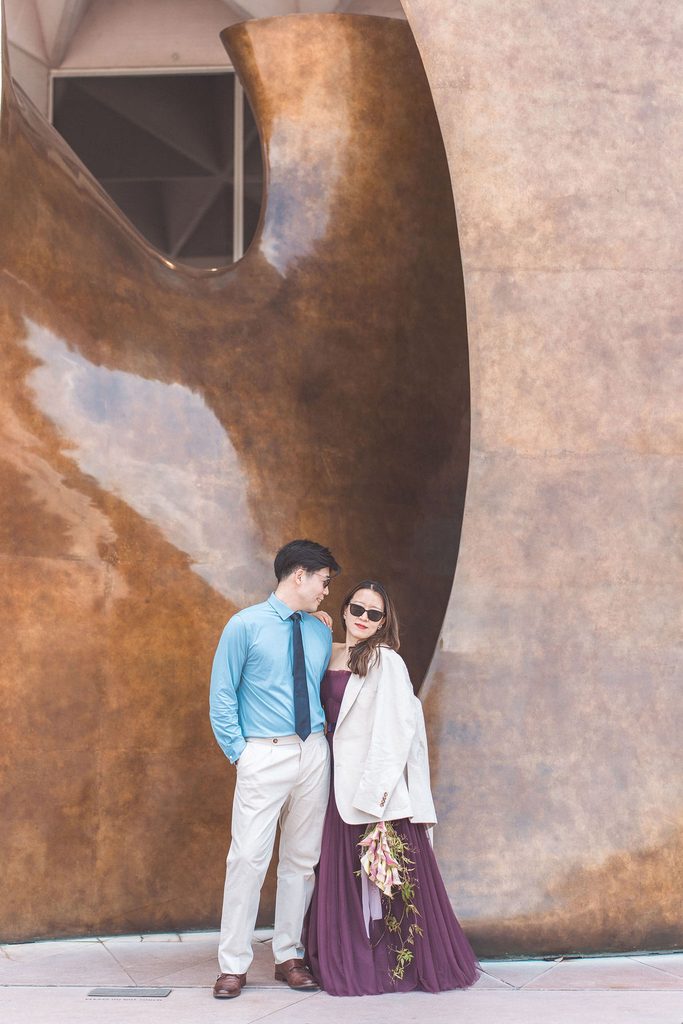 National Gallery of Art engagement photos of a couple posing in sunglasses beside a large bronze sculpture with a cascading floral bouquet.